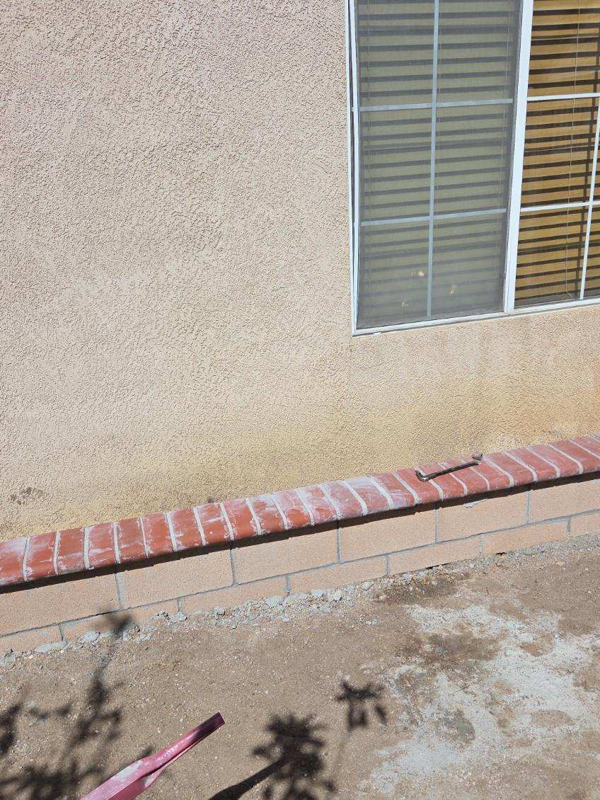 Red brick cap on a block wall beside a stucco house